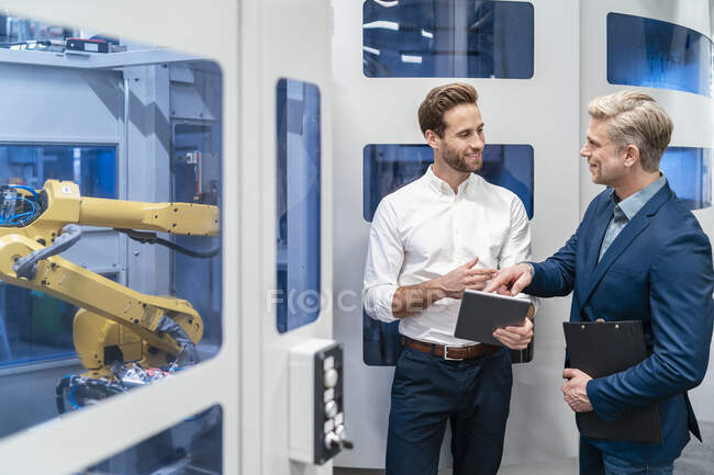 Two businessmen talking at robot in a modern factory — Stock Photo