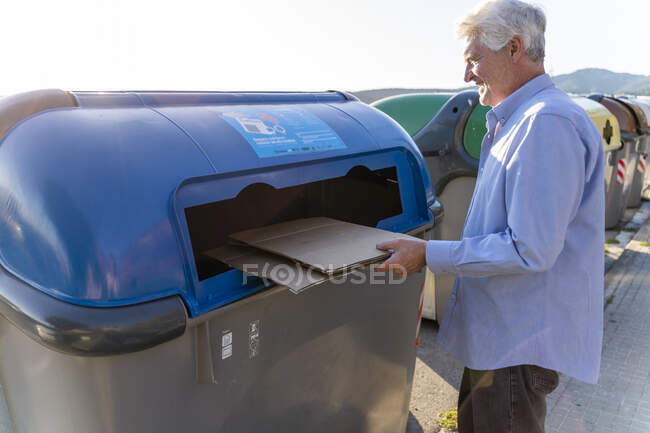 Senior man recycling cardboard in paper bank — Stock Photo