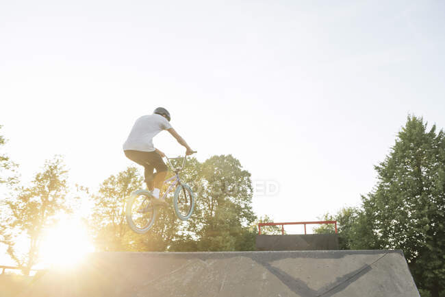 Jovem andar de bicicleta BMX no skatepark ao pôr do sol — Fotografia de Stock