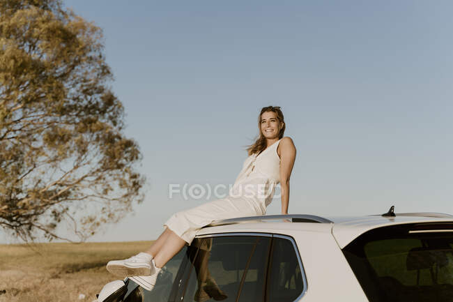 Feminino viajante sentado no telhado do carro branco — Fotografia de Stock