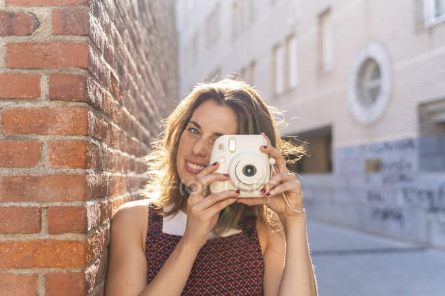 Giovane donna appoggiata al muro di mattoni, utilizzando la fotocamera — Foto stock