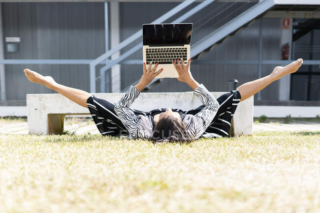 Female ballet dancer doing a spagat in front of an office, using laptop lying — Stock Photo