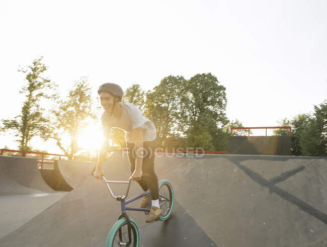 Jovem feliz andando de bicicleta BMX no skatepark ao pôr do sol — Fotografia de Stock