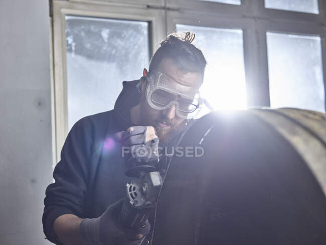Человек работает на металлическом контейнере с шлифовальным станком — стоковое фото