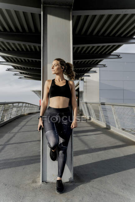 Sporty woman with headphones standing on bridge, listening music, using smartphone — Stock Photo