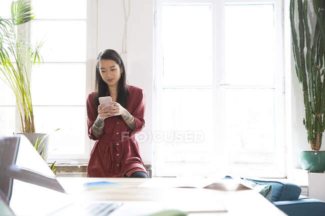 Женщина, использующая мобильный телефон у окна в офисе — стоковое фото