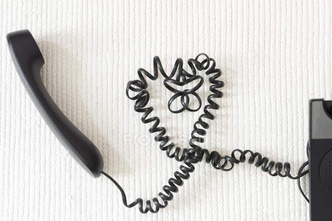 Cable de teléfono negro en forma de corazón en suelo blanco - foto de stock