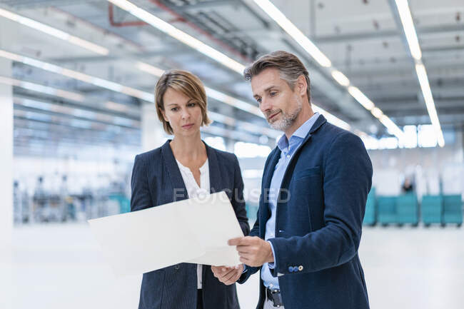 Businessman and businesswoman discussing plan in a factory hall — Stock Photo
