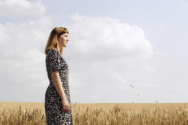 Giovane donna che indossa abito con disegno floreale in piedi nel campo di grano — Foto stock