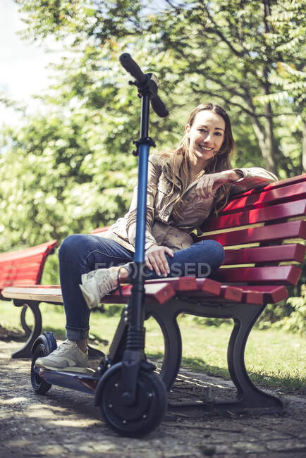 Портрет улыбающейся женщины с E-Scooter расслабляющий на скамейке — стоковое фото