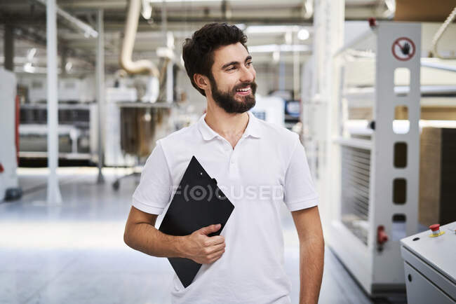 Lächelnder Mitarbeiter mit Klemmbrett in einer Fabrik — Stockfoto