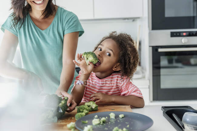 Ragazza cucina con mamma in cucina degustazione broccoli — Foto stock