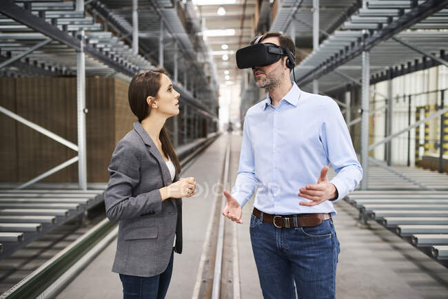 Geschäftsfrau spricht mit Geschäftsmann mit VR-Brille in Fabrik — Stockfoto