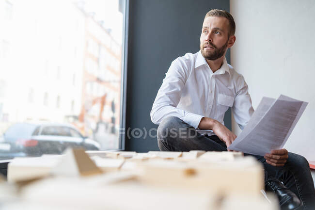 Geschäftsmann mit Papieren und Architekturmodell im Amt — Stockfoto