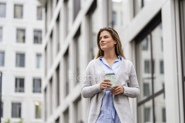 Jeune femme d'affaires avec café pour aller tasse, immeuble de bureaux en arrière-plan — Photo de stock