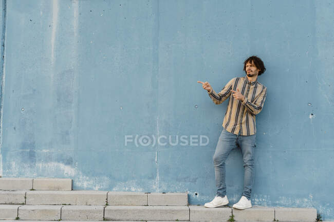 Bearded man wearing striped shirt standing ibn front of light blue wall gesticulating — Stock Photo