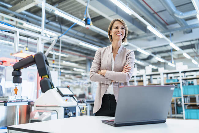 Donna d'affari sorridente con computer portatile in una moderna sala di fabbrica — Foto stock