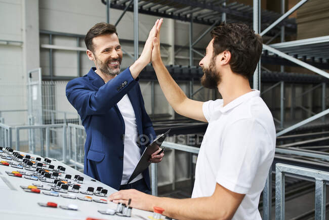 Happy businessman and employee high fiving at control panel in a factory — Stock Photo