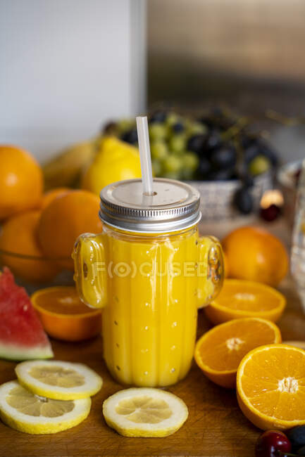 Batido de naranja en la mesa de la cocina con varias frutas - foto de stock