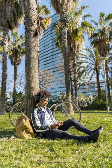 Uomo d'affari occasionale con bicicletta utilizzando il cellulare nel parco urbano, Barcellona, Spagna — Foto stock