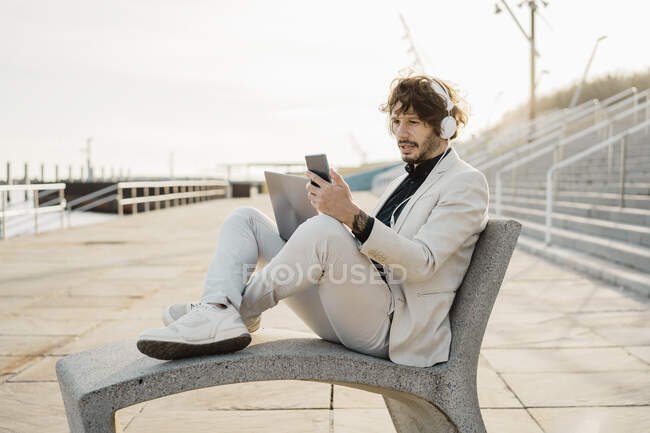 Portrait d'homme d'affaires choqué avec écouteurs et ordinateur portable regardant son téléphone portable — Photo de stock