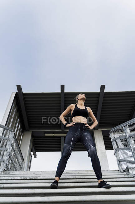 Donna sportiva in piedi sulle scale, con le mani sui fianchi — Foto stock