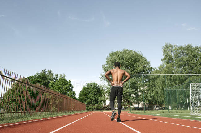 Homme sportif marchant sur un hippodrome en caoutchouc, vue arrière — Photo de stock