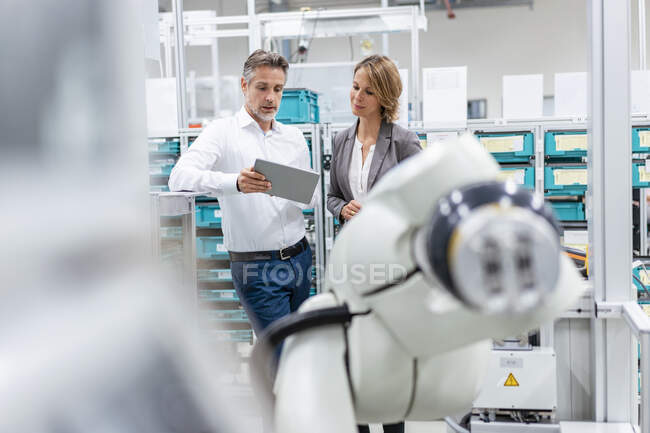 Uomo e donna d'affari con tablet che parlano al robot di assemblaggio in una fabbrica — Foto stock