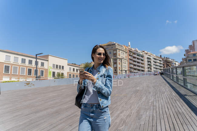 Молодая женщина с помощью смартфона на пешеходном мосту в Барселоне — стоковое фото