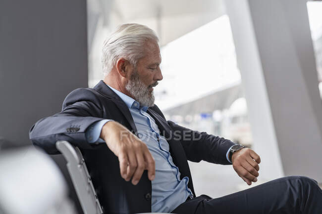 Mature businessman sitting in waiting area checking the time — Stock Photo