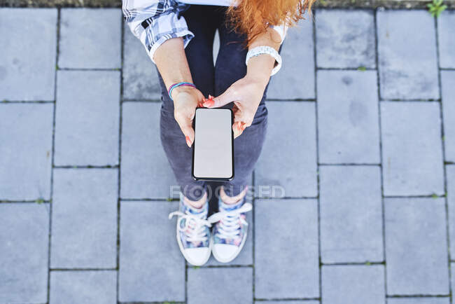 Vue du dessus de la femme utilisant un smartphone assis à l'extérieur — Photo de stock