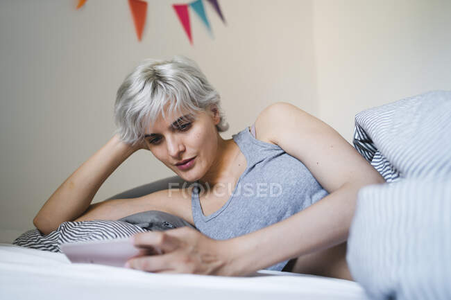 Frau liegt mit Handy im Bett — Stockfoto