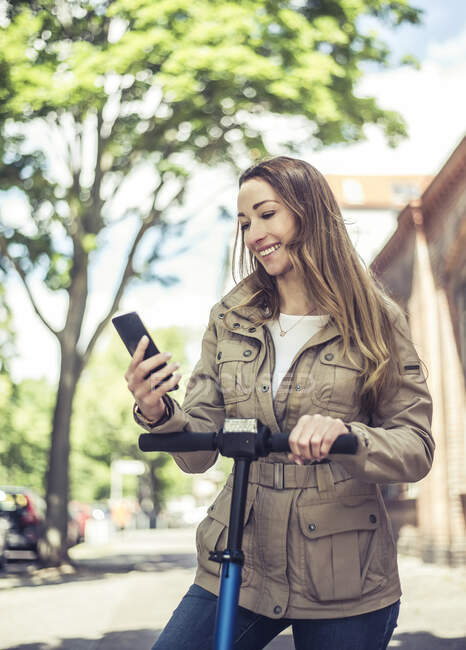 Портрет улыбающейся женщины со скутером, смотрящей на смартфон — стоковое фото