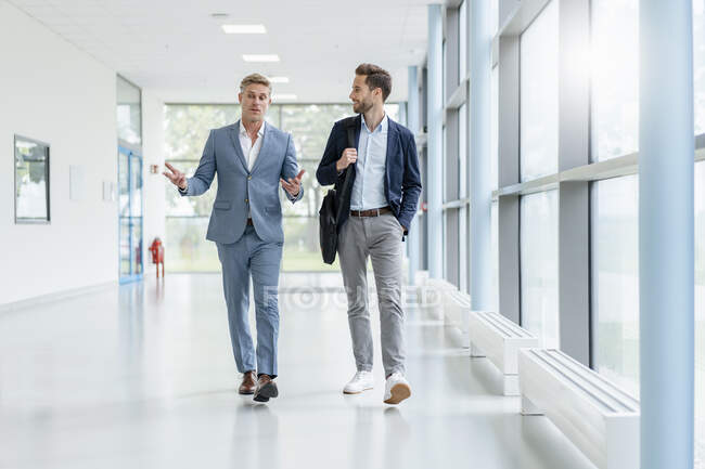 Dos hombres de negocios caminando y hablando en un pasillo - foto de stock