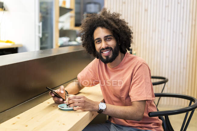 Portrait of a smiling man with cell phone sitting at the counter of a bar — Stock Photo