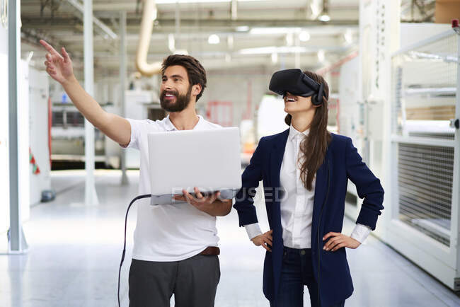 Man with laptop and businesswoman wearing VR glasses in factory — Stock Photo