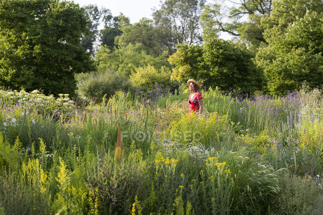 Mujer con sombrero de paja y vestido rojo de verano en el jardín con flores silvestres - foto de stock