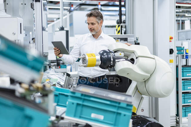 Бизнесмен с планшетом на сборочном роботе на заводе — стоковое фото