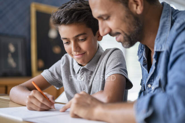 Усміхаючись, батько допомагає синові виконувати домашнє завдання. — стокове фото