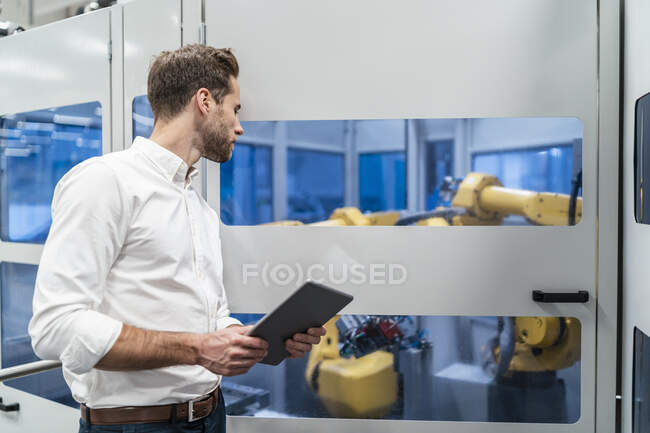 Бизнесмен с планшетом смотрит на робота на современном заводе — стоковое фото