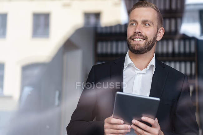 Smiling businessman with tablet looking out of window — Stock Photo