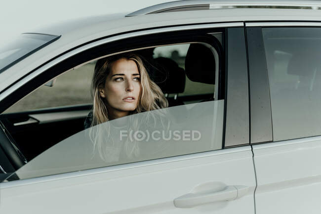 Blond woman in white car looking out of the window — Stock Photo
