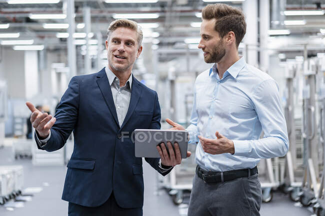 Due uomini d'affari con tablet che parlano in una fabbrica moderna — Foto stock