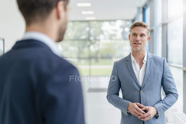 Empresario en un pasillo hablando con su colega - foto de stock