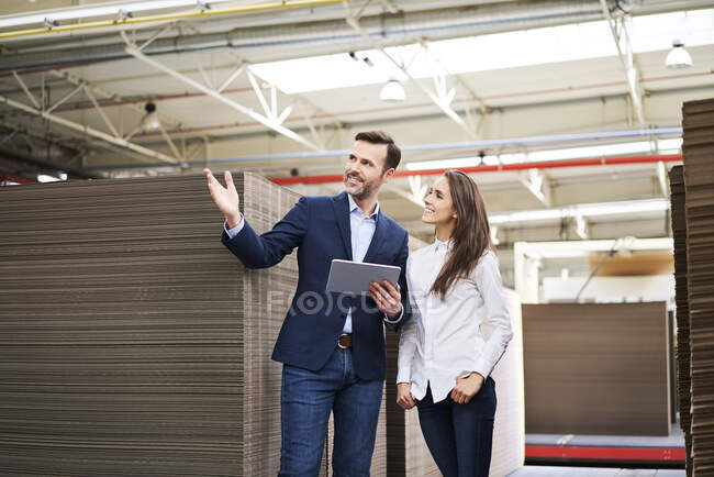 Empresario con tableta hablando con mujer en almacén de fábrica - foto de stock