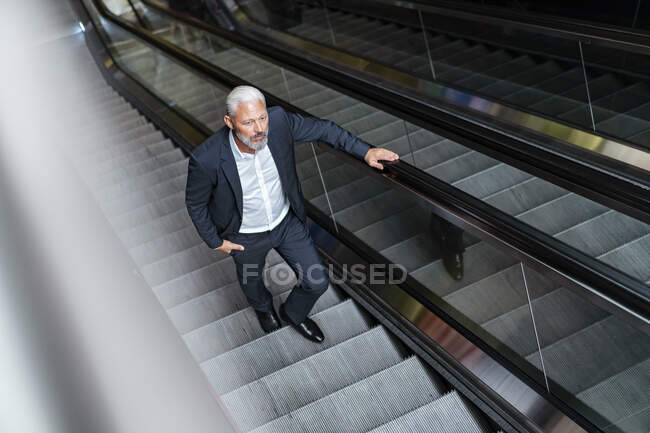 Maduro hombre de negocios en una escalera mecánica - foto de stock