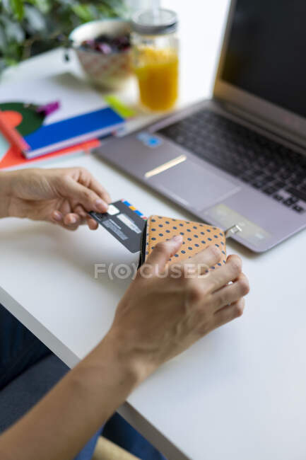 Close-up de mulher com laptop tirando cartão da bolsa na mesa — Fotografia de Stock