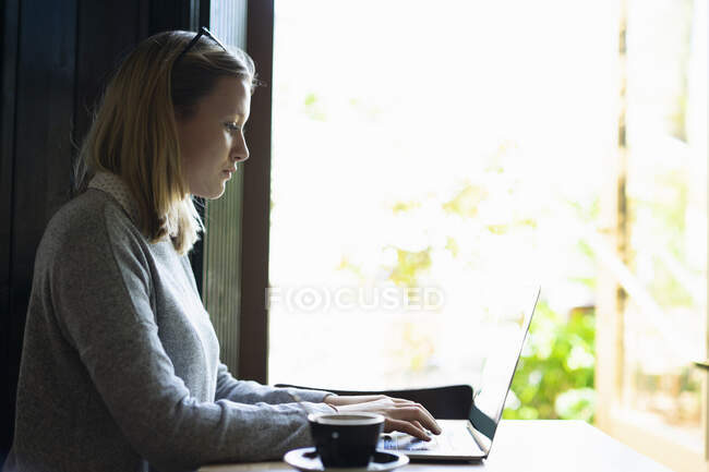 Jeune femme utilisant un ordinateur portable dans un café — Photo de stock