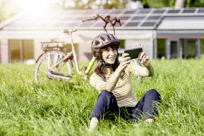 Щаслива жінка сидить на лузі з велосипедом, приймаючи селфі — стокове фото