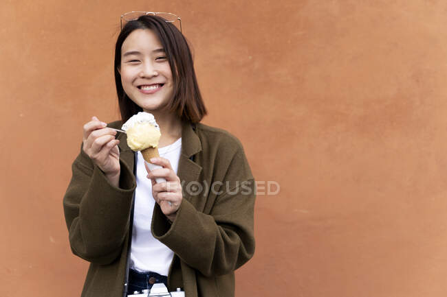 Happy young woman eating an ice cream cone at an orange wall — Stock Photo